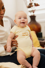 Baby smiling in a woman's lap, wearing the WeNatal x Tabeeze Bottom Up Bodysuit, showcasing comfort and practicality for easy changing and bonding.
